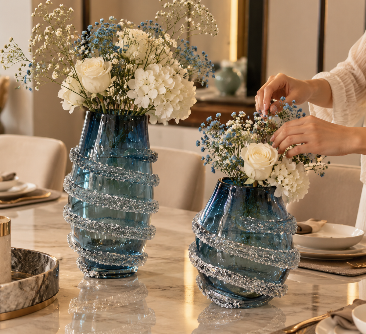 Two sculptural blue vases with sparkling silver-tone spiral embellishments, styled with white flowers and blue baby's breath.